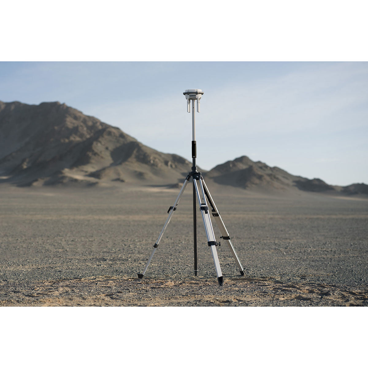 DJI D-RTK 3 Multifunctional Station mounted on a survey tripod on open ground with mountains behind it