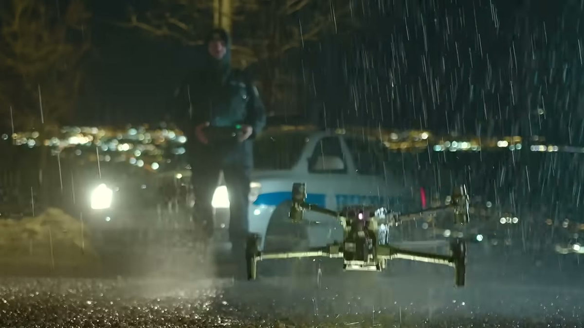 DJI Matrice 30T taking off in heavy rain at night beside a police car